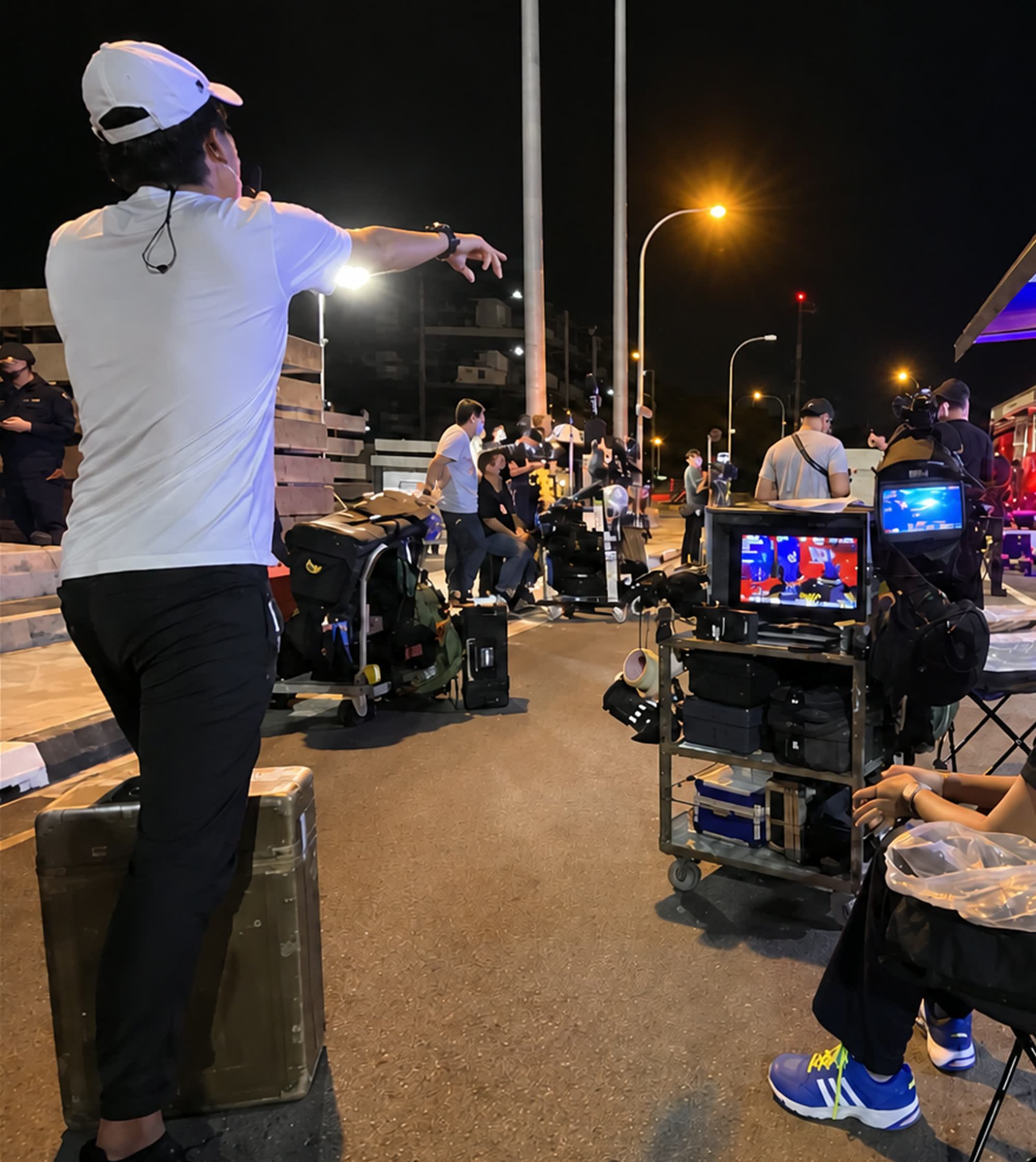 A film crew working at night on a road, with monitors, carts and equipment cases